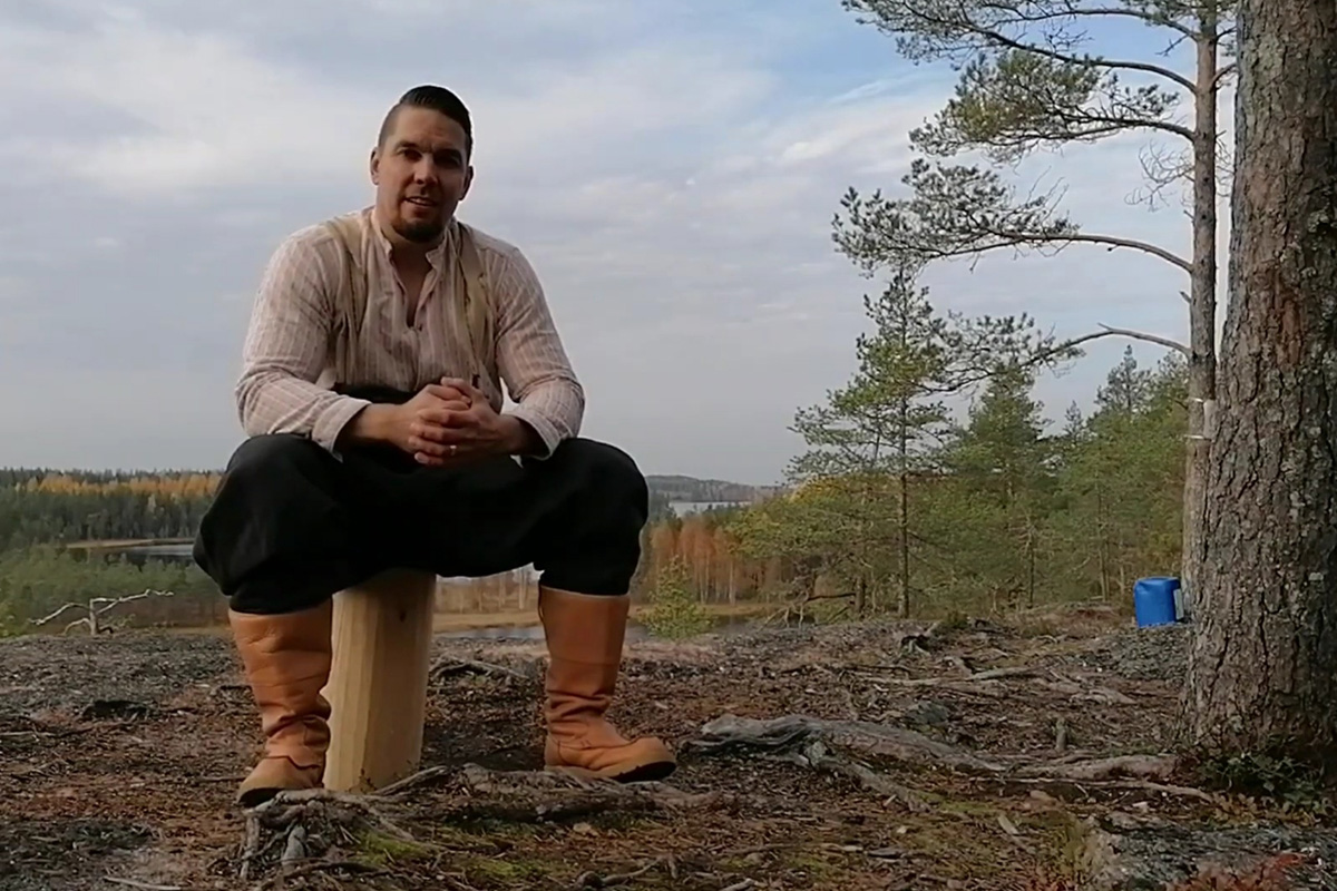 Marko Pehkonen istuu metsässä, taustalla kaunis luontomaisema